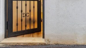 Une entrée d’immeuble avec un portail en métal noir et une fenêtre ornée de barreaux verticaux.
