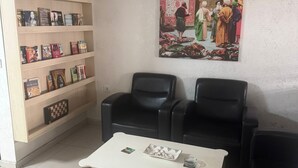 Un soggiorno con un tavolino da caffè bianco, poltrone in pelle nera, una libreria piena di libri, una ventola a soffitto e un grande quadro appeso al muro.