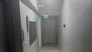 Un corridoio stretto e ben illuminato con pavimento in legno, una porta in fondo e un rilevatore di fumo a parete.