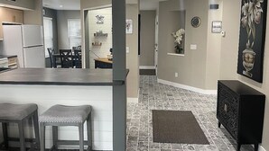 Una cocina moderna con barra, una mesa de comedor y sillas. Hay un reloj en la pared y un cuadro sobre la puerta.