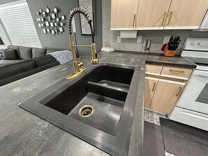 A modern kitchen with a black sink, stainless steel appliances, and wooden cabinets.