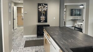 Una cocina moderna con encimera oscura, piso de baldosas y un cuadro de flores en la pared.