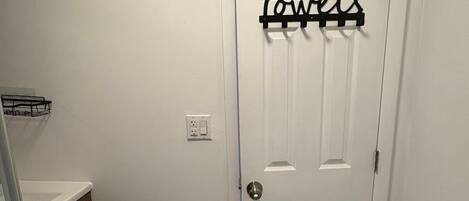 A bathroom with a white door, a towel rack with the word "Towels" on it, a small painting on the wall, and a shower area with a glass door.