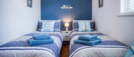 A bedroom with two beds, each with blue towels and nautical-themed pillows.