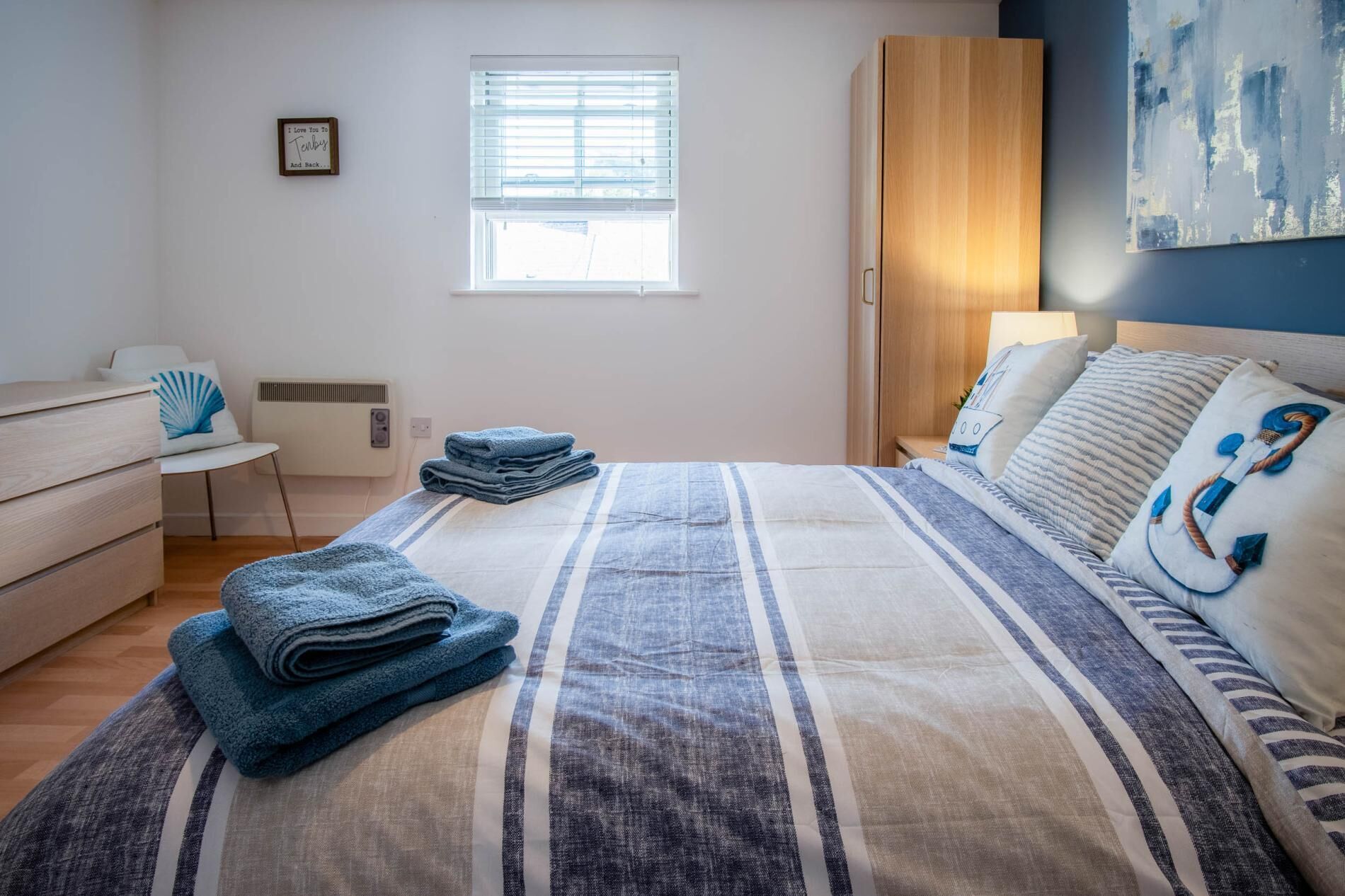 A bedroom with a bed, a nightstand, a dresser, a window, and a painting on the wall.