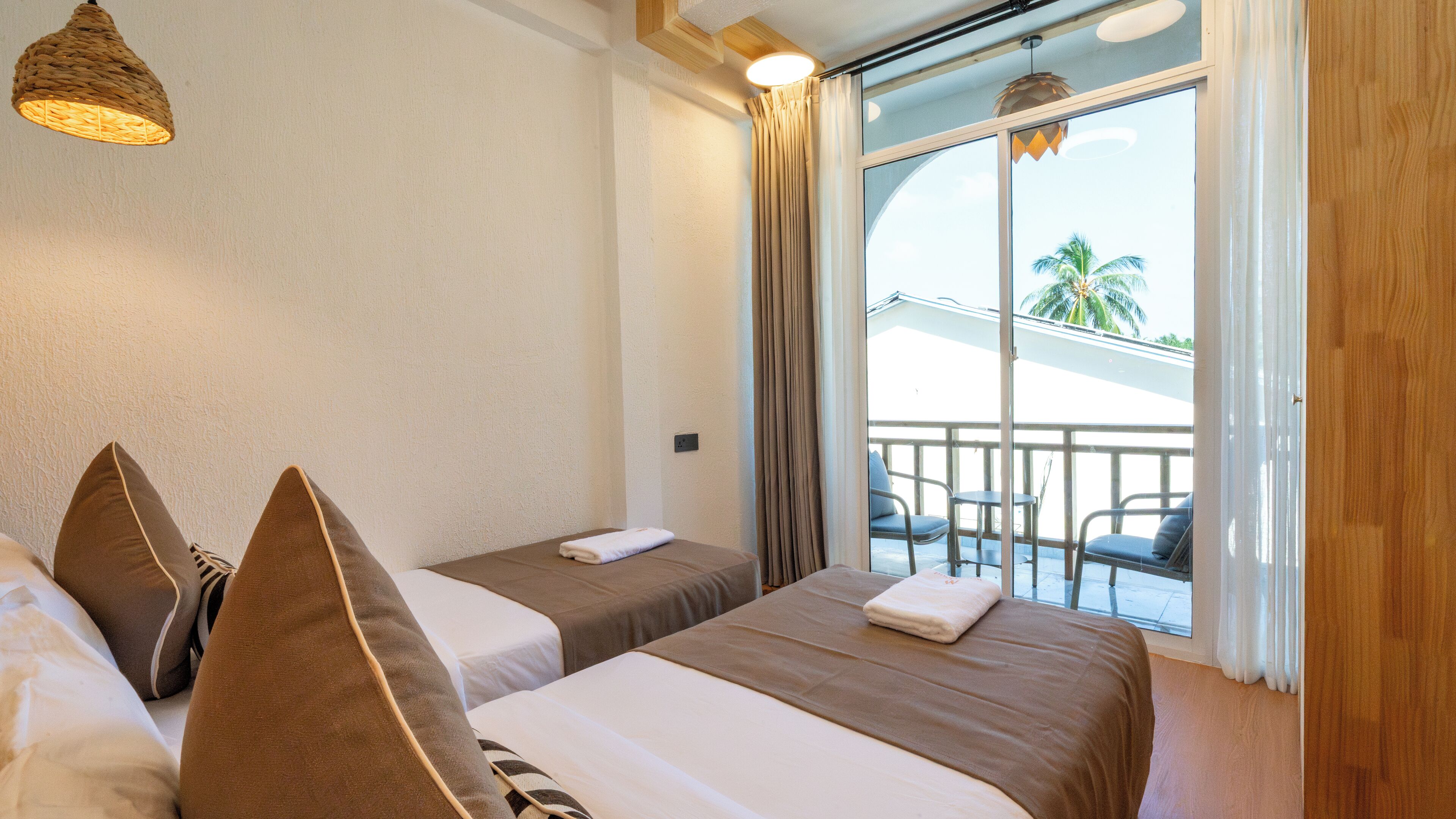 A hotel room with two beds, a balcony with chairs, and a view of palm trees.
