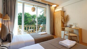 A hotel room with two beds, a balcony with a chair, a wooden desk with a chair, and a large window with curtains.