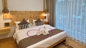 Un dormitorio ordenado con cabecera de madera, cama con toalla con forma de cisne y un ventanal con cortinas traslúcidas.