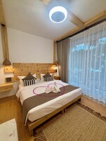 Un dormitorio ordenado con cabecera de madera, cama con toalla con forma de cisne y un ventanal con cortinas traslúcidas.