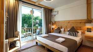 Un dormitorio con una cama grande, cabecera de madera, balcón con una silla y vistas a árboles.