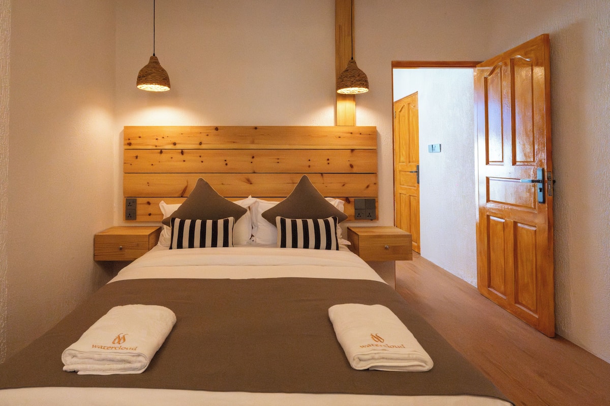 A neatly made bed with striped pillows, a wooden headboard, and two bedside tables with lamps.