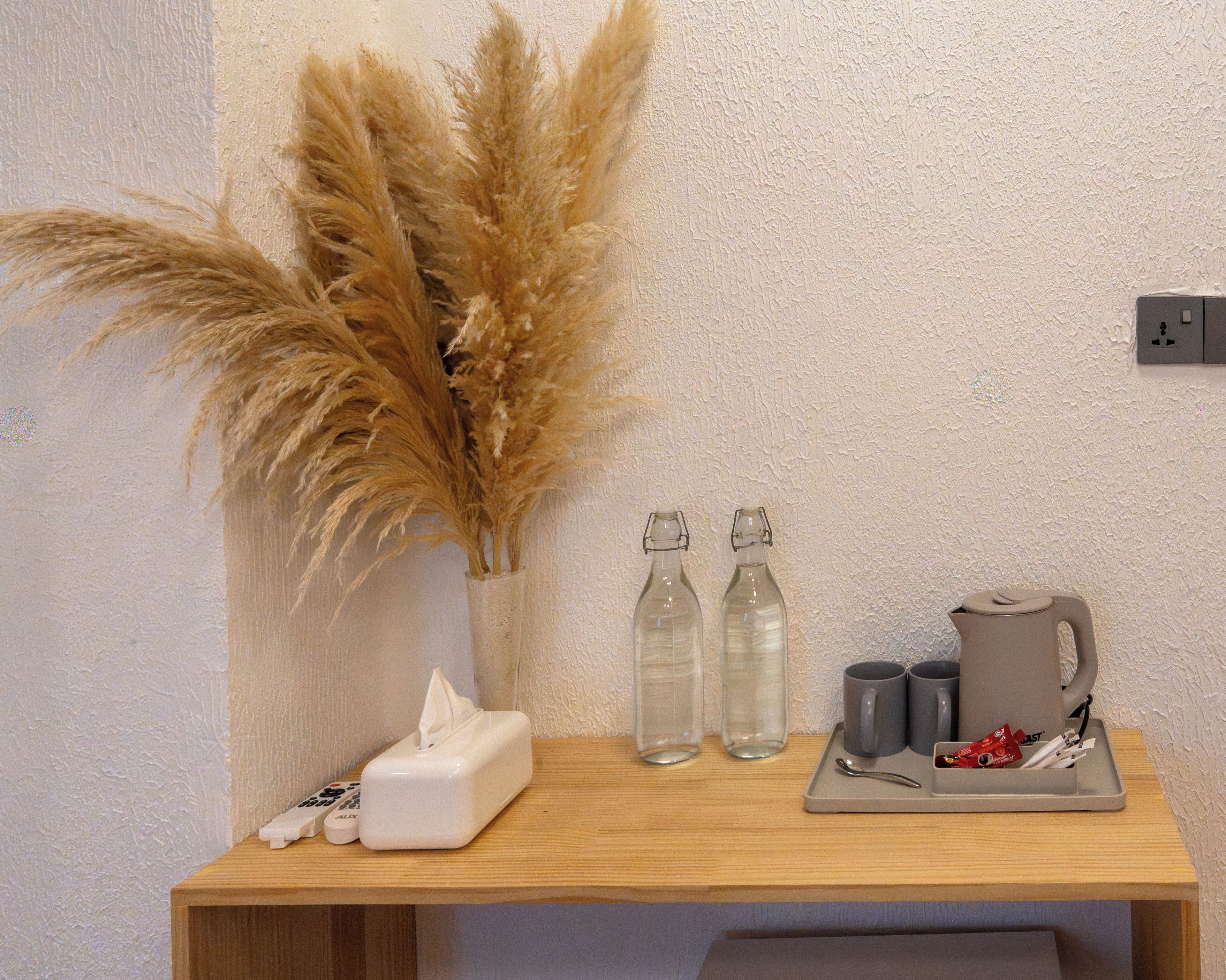 A wooden table with a tissue box, two glass bottles, a mug, and a kettle.