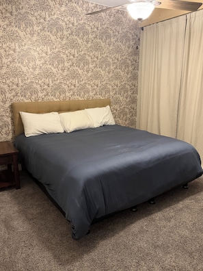 Una camera da letto con un letto, un comodino, una ventola a soffitto e una finestra con tende.