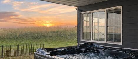 Un jacuzzi bajo un porche techado con vista a un campo de hierba al atardecer.