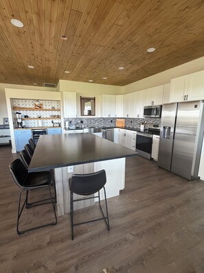 A modern kitchen with a large island, stainless steel appliances, and a wooden ceiling.