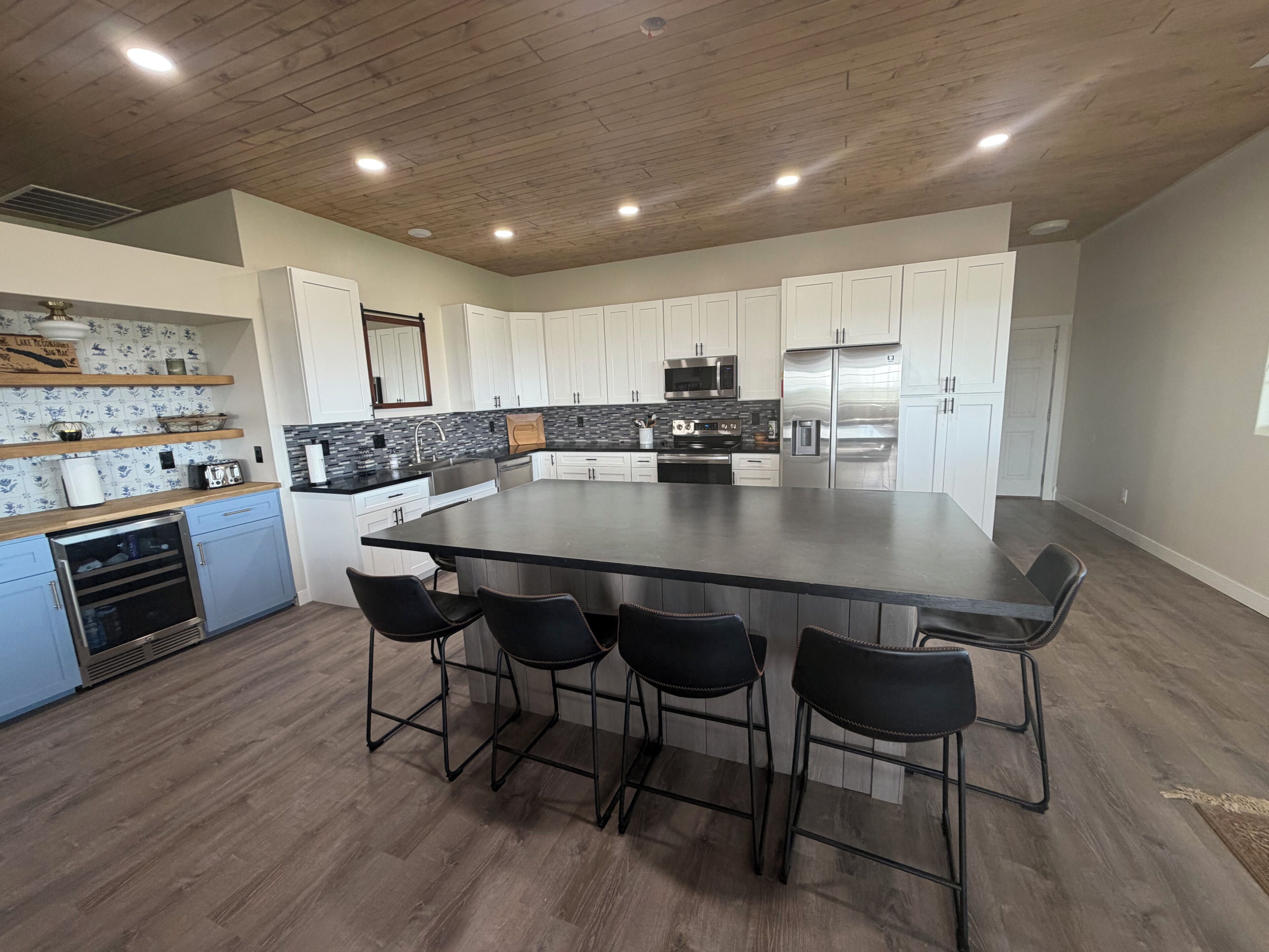 Una cocina moderna con una isla grande, armarios blancos, electrodomésticos de acero inoxidable y techo de madera.