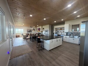 Een ruime keuken met een centraal eiland, houten vloeren en witte kasten.