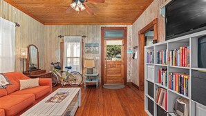 Une pièce avec un plafond en bois, un ventilateur de plafond, une bibliothèque remplie de livres, un vélo, un canapé en bois et un téléviseur.