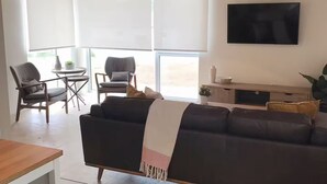 Una sala de estar moderna con un sofá oscuro, una mesa de comedor de madera y un televisor montado en la pared.