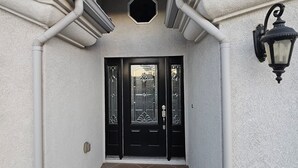 Entrada de un edificio con puerta negra, letrero de seguridad y farola.