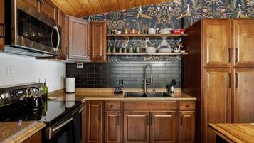 A kitchen with wooden cabinets, a stainless steel range, a black tiled backsplash, and a wooden countertop.