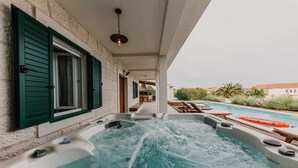 A hot tub area with a view of a swimming pool and a building with green shutters. - Villa Del Tempo with Pool (Seget Donji)