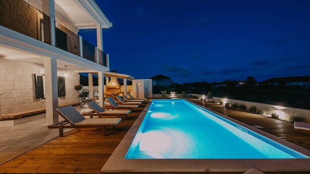 A rectangular pool with lounge chairs and a barbecue area, surrounded by a wooden deck and stone walls. - Villa Del Tempo with Pool (Seget Donji)