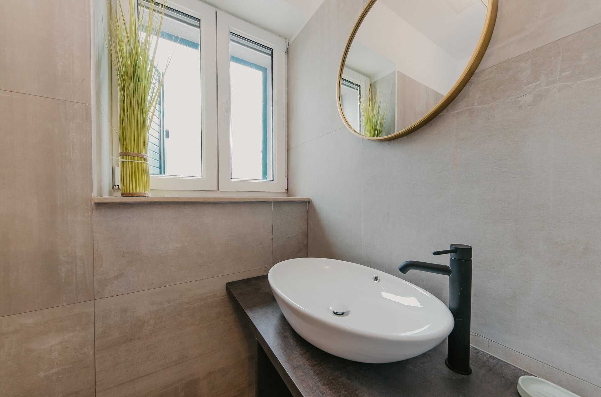 A modern bathroom with a white sink, dark countertop, and a round mirror.