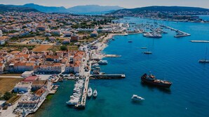 An aerial view of a coastal town with a marina filled with boats, a large ship docked, and a mix of residential and commercial buildings. - Villa Del Tempo with Pool (Seget Donji)