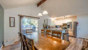Una cocina moderna con una mesa de comedor de madera, armarios blancos, electrodomésticos de acero inoxidable y un amplio ventanal.