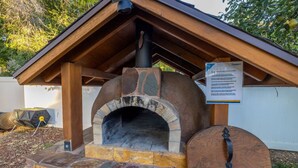 Un horno para pizza de piedra con chimenea, bajo una estructura de techo de madera.