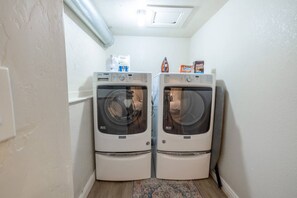 A laundry room with two front-loading washing machines, a small shelf with detergent, and a patterned rug on the floor.
