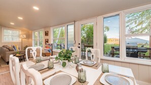 Comedor con mesa preparada para cuatro personas, rodeado de grandes ventanales con vistas al exterior.