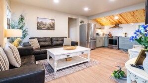 Una sala moderna con un sofá de cuero, una mesa de centro blanca y una cocina equipada con electrodomésticos de acero inoxidable.