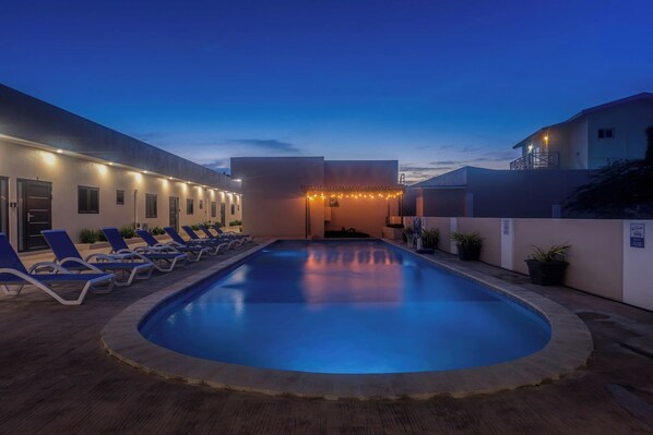 A swimming pool with lounge chairs and a building with lights. - Palm Beach Hideaway #2: 2BR Condo, Private Patio to Pool & Rooftop (Noord)
