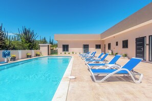 A swimming pool with lounge chairs and a building with multiple windows and doors. - Palm Beach Hideaway #2: 2BR Condo, Private Patio to Pool & Rooftop (Noord)