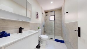 A modern bathroom with a white sink, toilet, and glass-enclosed shower. - Palm Beach Hideaway #2: 2BR Condo, Private Patio to Pool & Rooftop (Noord)