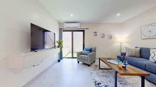 A modern living room with a flat-screen TV, a sofa, a patterned armchair, and a coffee table.