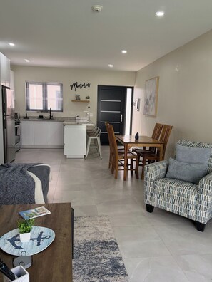 A modern kitchen with a dining area, a sofa, and a coffee table with a book and a plant.