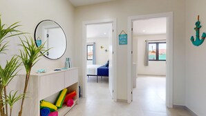 A hotel room with a bed, a bathroom with a mirror, a plant, and a hallway leading to another room.