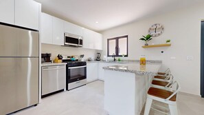A modern kitchen with stainless steel appliances, a central island with bar stools, and a clock on the wall.
