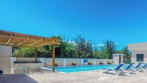 A pool area with lounge chairs, a pergola, and a small building.
