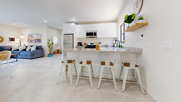 A modern kitchen with white cabinets, a microwave, and a stainless steel range hood. There are four bar stools in front of the kitchen island.