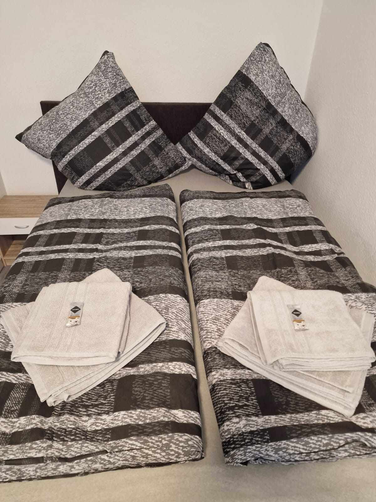 Een keurig opgemaakt bed met een gestreept laken en twee kussens, elk met een geometrisch patroon.