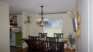 A dining area with a wooden table, chairs, a chandelier, and a window with blinds. - Relaxing Country Getaway – Pet Friendly, Close to Greenville & Spartanburg (Greer)