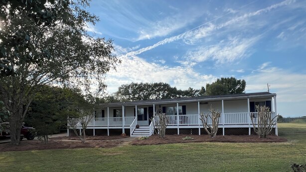 A single-story house with a porch, surrounded by a grassy yard and trees. - Relaxing Country Getaway – Pet Friendly, Close to Greenville & Spartanburg (Greer)