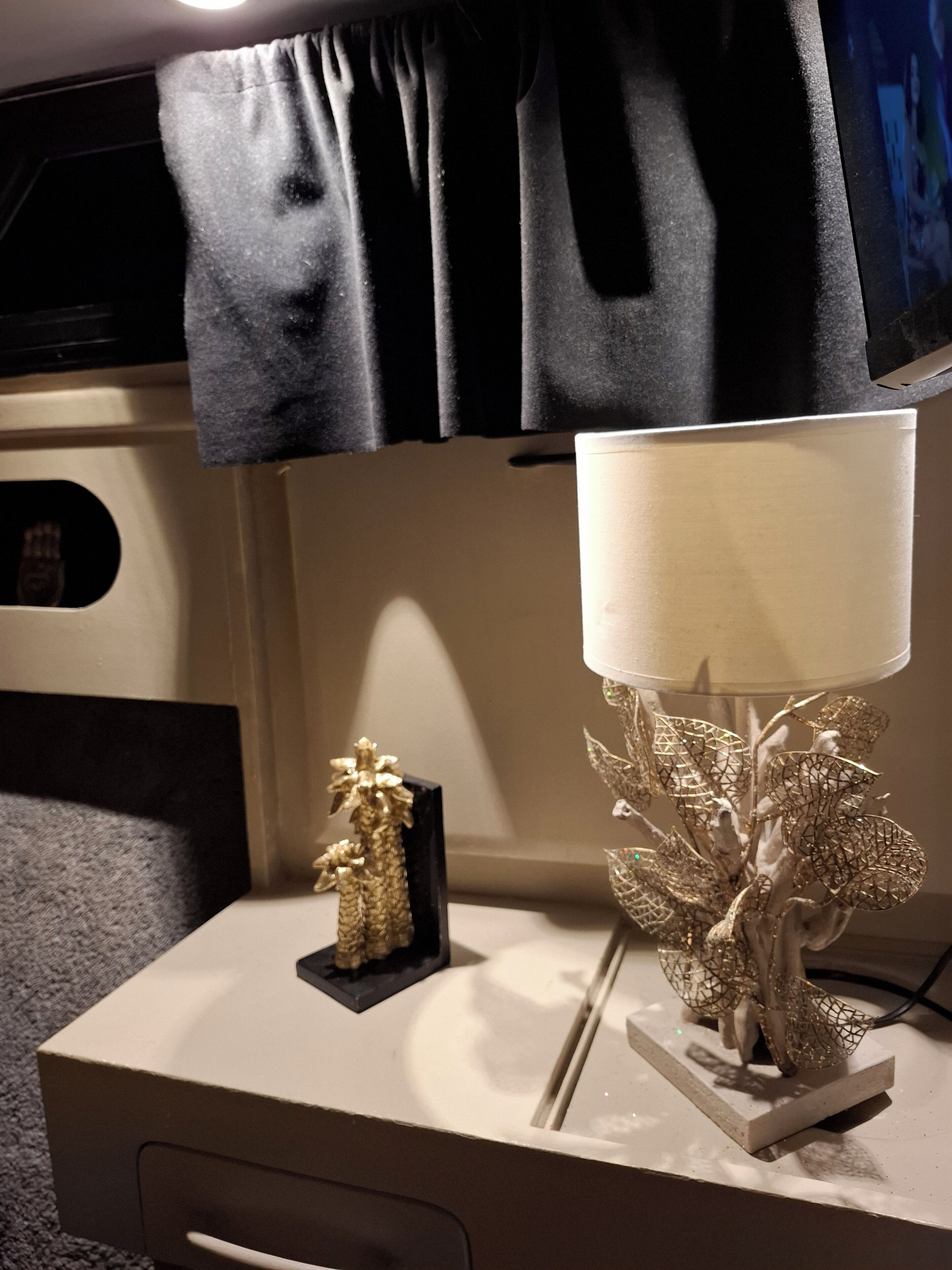 Et natbord med en lampe, en dekorativ guldfigur og en sort genstand på væggen.