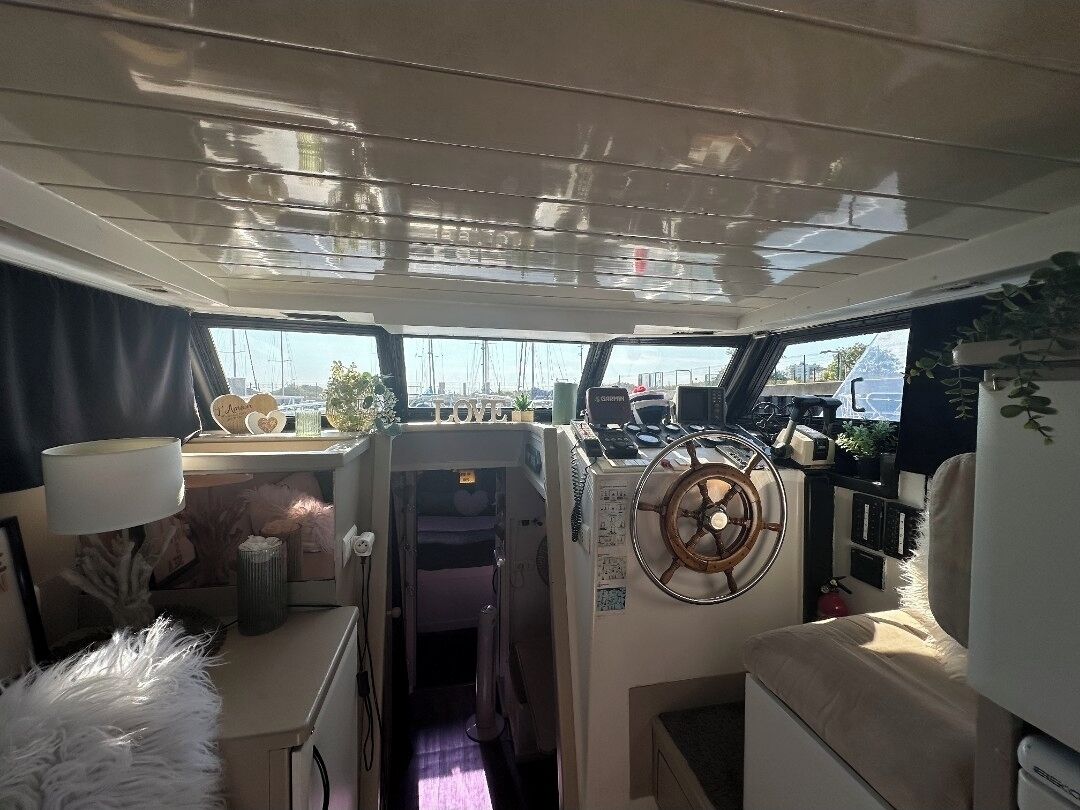 A boat's interior with a steering wheel, a control panel, and a view of the outside.