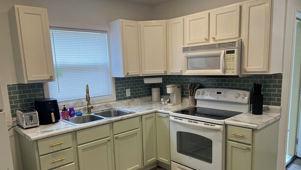 A kitchen with white cabinets, a microwave, a stove, and a sink.