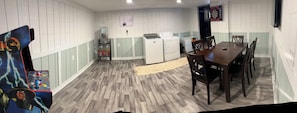 A compact room with a dining table and chairs, a washing machine, a small refrigerator, and a dartboard on the wall. - Beautiful apt, serene design in Bay City-Perfect for a getaway,close to downtown (Bay City)